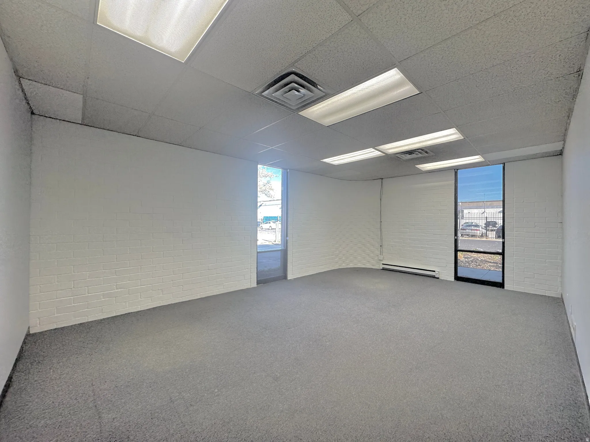 Carpeted empty room featuring a drop ceiling and a baseboard radiator