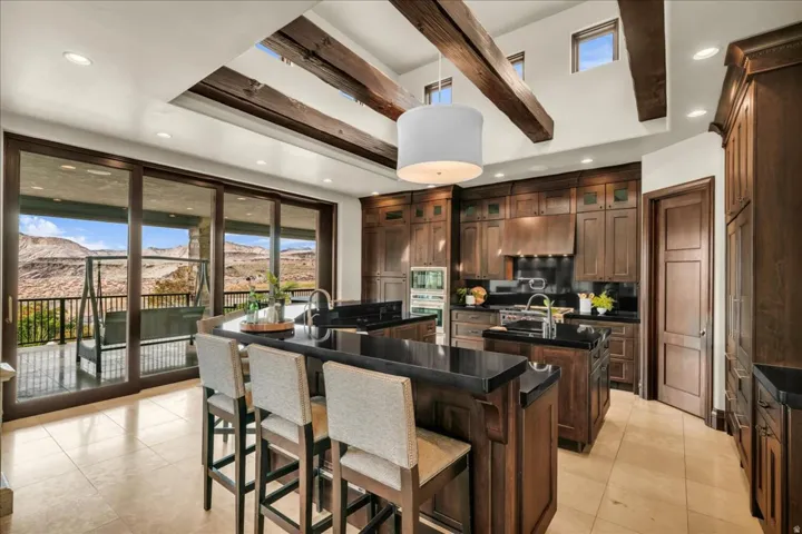 Kitchen featuring a breakfast bar, pendant lighting, beam ceiling, stainless steel appliances, and under cabinet range hood