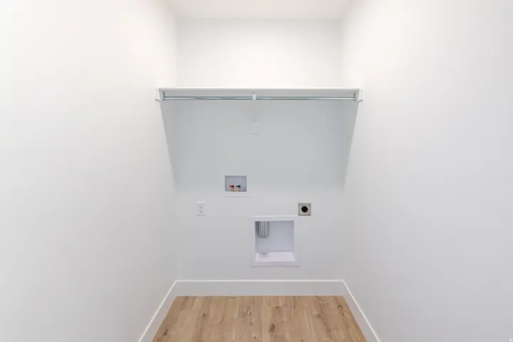 Dedicated laundry area featuring wood-finish flooring, crisp white walls, and a built-in shelving unit with a hanging rod