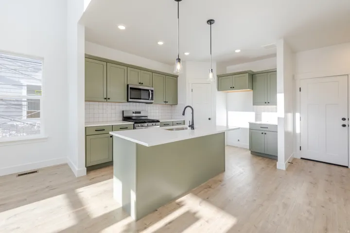 Kitchen featuring sage green cabinetry, stainless steel appliances, a white tile backsplash, and a central island with a white countertop