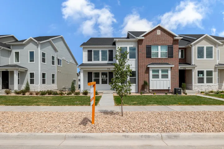 Contemporary townhouse with a brick and siding facade, featuring dark-framed windows, decorative shutters, a paved walkway, and a manicured lawn