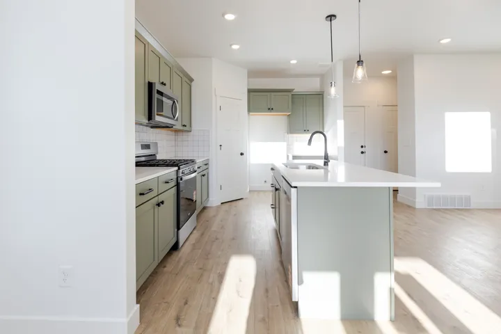 Kitchen featuring sage green cabinetry, stainless steel appliances, white subway tile backsplash, a central island with a white countertop and integrated sink, and wood-finish flooring