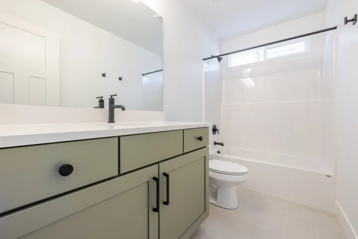 Modern bathroom featuring a sage green vanity with matte black hardware, a white countertop, and an integrated rectangular sink