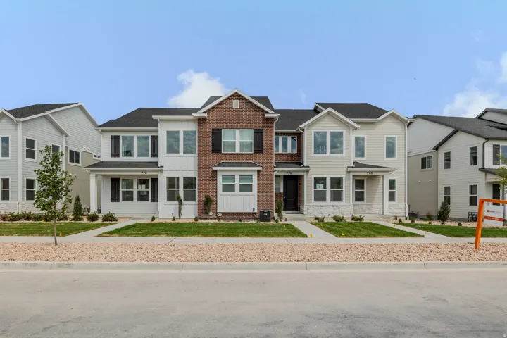 Contemporary townhome facade featuring a prominent brick and siding exterior, multi-pane windows, dark shutters, and a covered entry