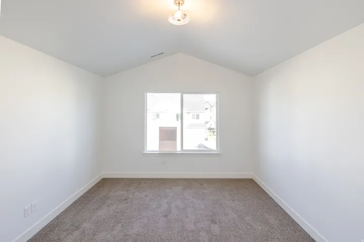Room featuring a vaulted ceiling with a central flush-mount light fixture, a large window, neutral carpeting, and white baseboards