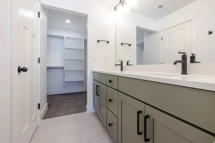 Bathroom vanity featuring dual sinks with matte black fixtures, light-toned countertop, and sage green cabinetry with black hardware
