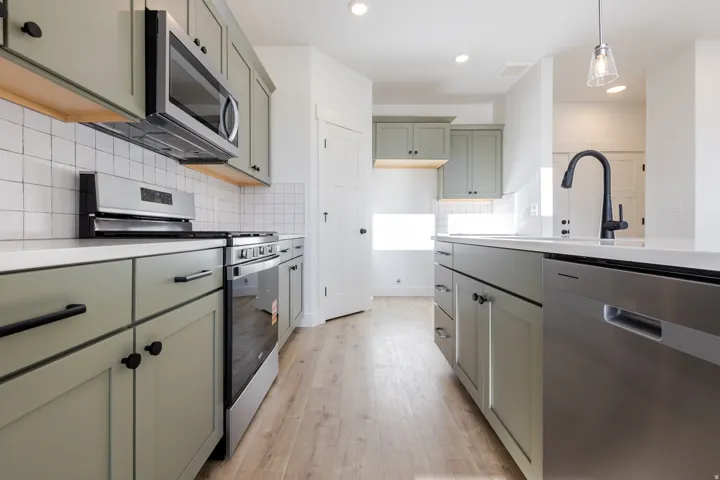 Kitchen featuring sage green cabinetry, stainless steel appliances, light-toned wood-finish flooring, white subway tile backsplash, and white countertops