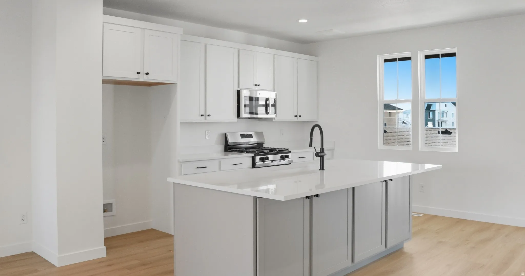 Kitchen with white cabinets, stainless steel appliances, a center island with sink, light wood-type flooring, and light stone counters