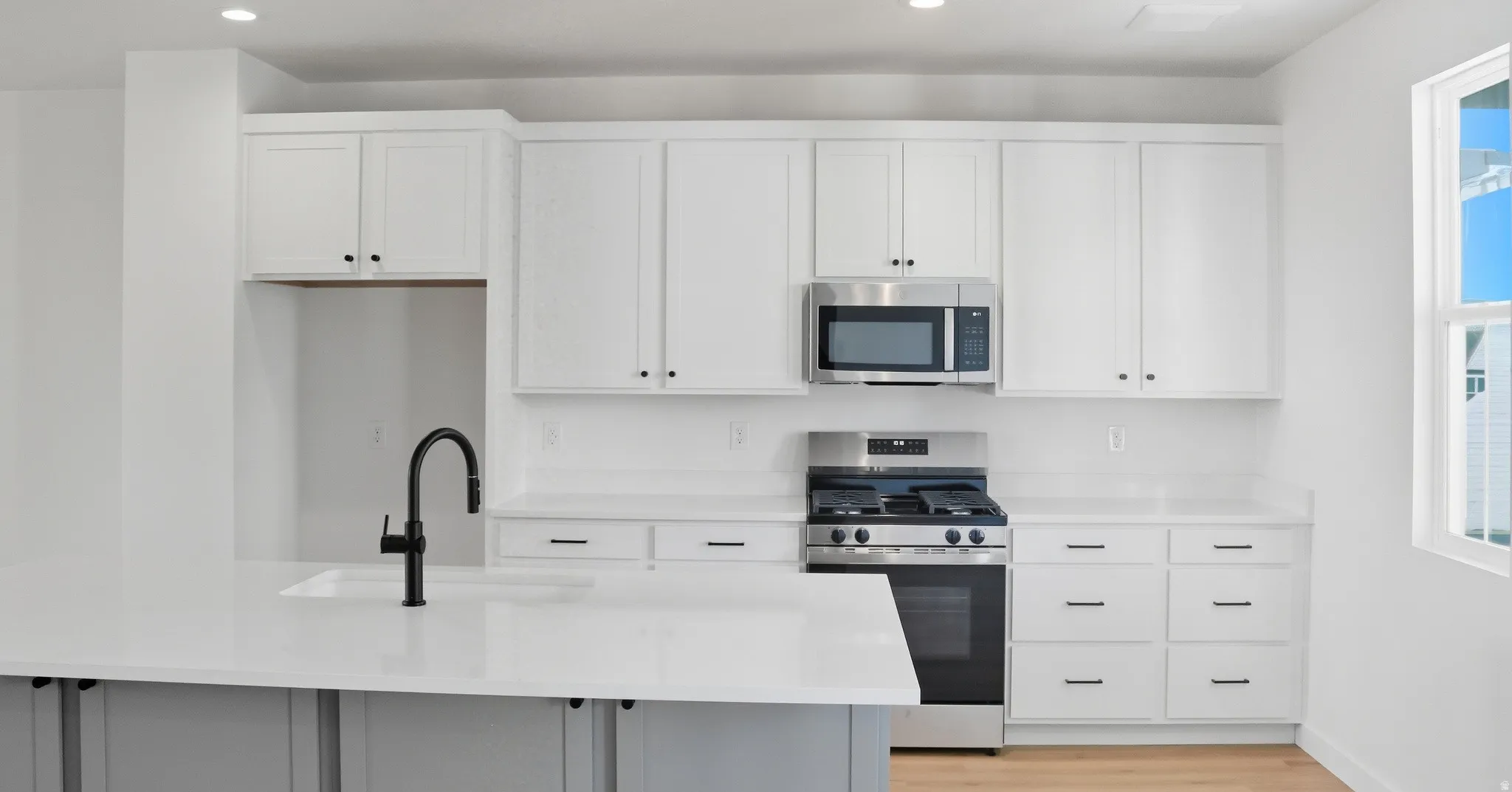 Kitchen featuring stainless steel appliances, white cabinets, recessed lighting, light stone counters, and plenty of natural light