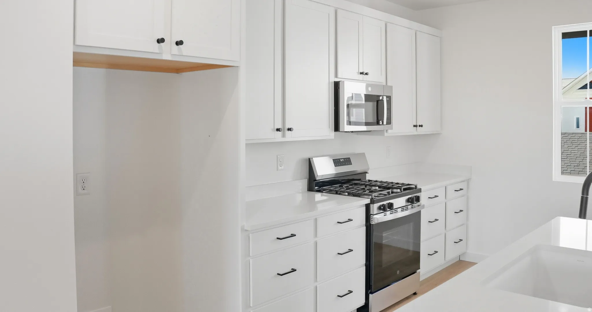 Kitchen with appliances with stainless steel finishes, white cabinets, light stone counters, and light wood-type flooring
