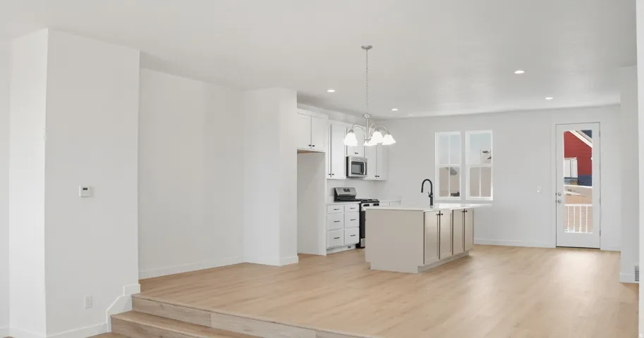 Kitchen featuring hanging light fixtures, appliances with stainless steel finishes, a chandelier, white cabinets, and light wood-style flooring