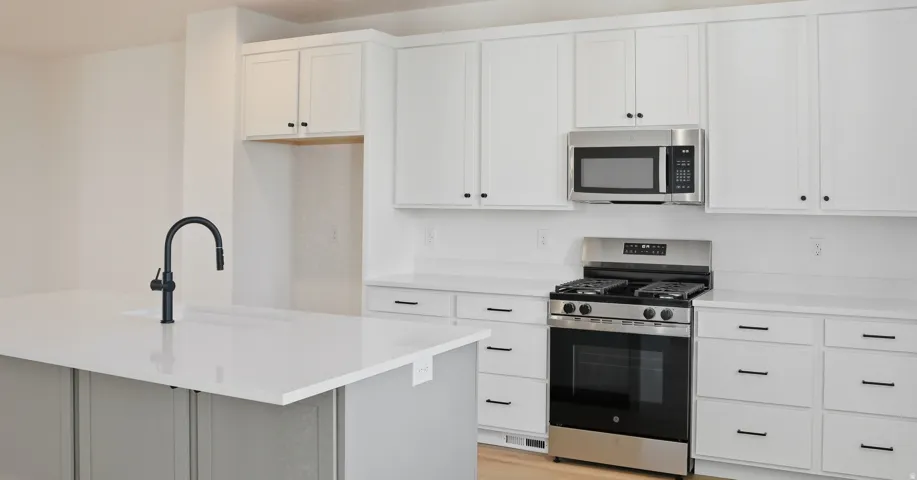 Kitchen featuring appliances with stainless steel finishes, white cabinets, an island with sink, light stone counters, and light wood-type flooring