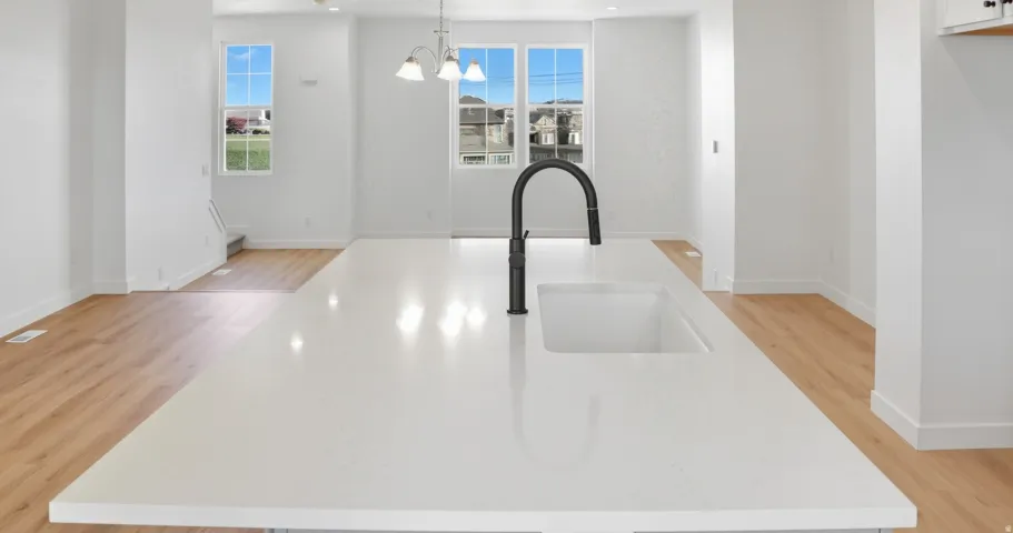 Kitchen view of a center island with sink, hanging light fixtures, light wood-type flooring, light stone countertops, and a chandelier
