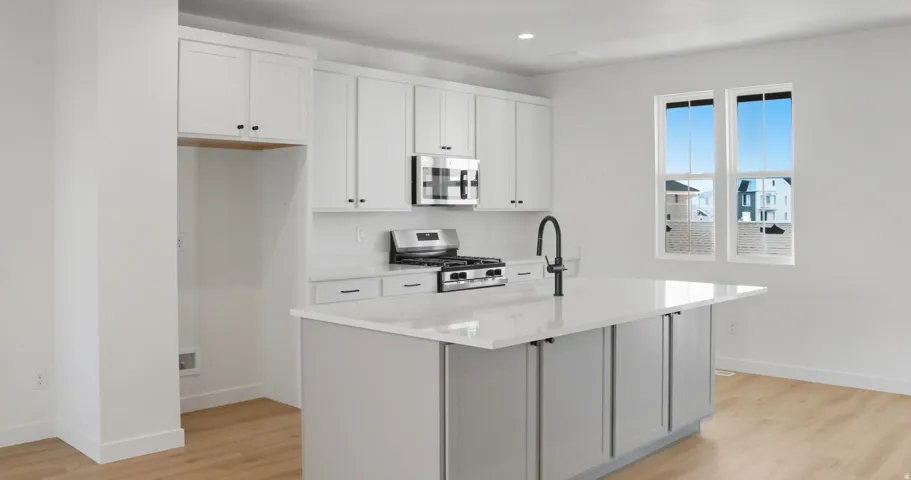 Kitchen with white cabinets, stainless steel appliances, a center island with sink, light wood-type flooring, and light stone counters