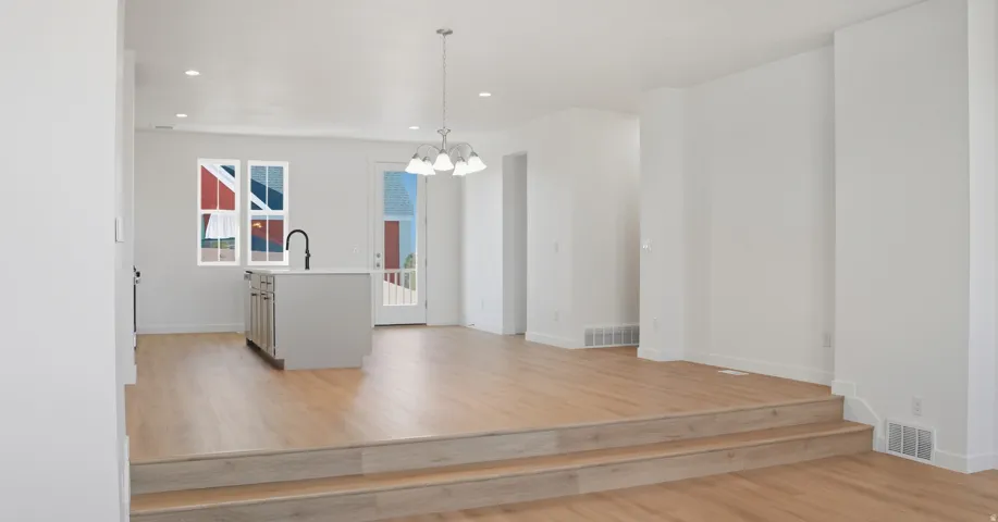 Kitchen featuring light wood finished floors, light countertops, hanging light fixtures, a center island with sink, and a chandelier