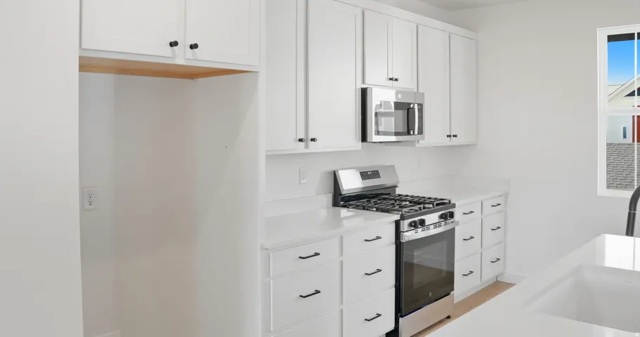 Kitchen with appliances with stainless steel finishes, white cabinets, light stone counters, and light wood-type flooring