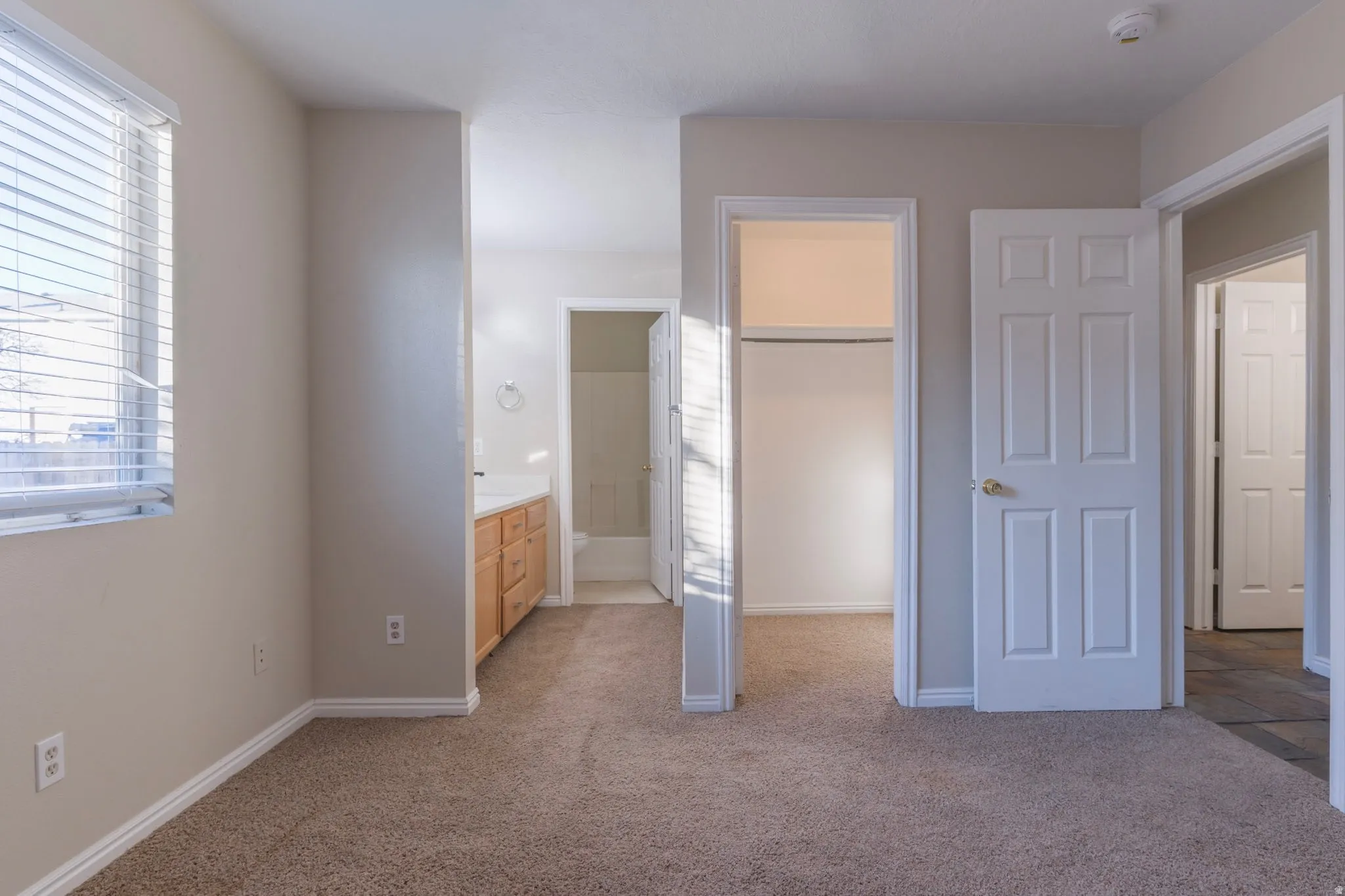 Unfurnished bedroom with light colored carpet, a walk in closet, and ensuite bathroom