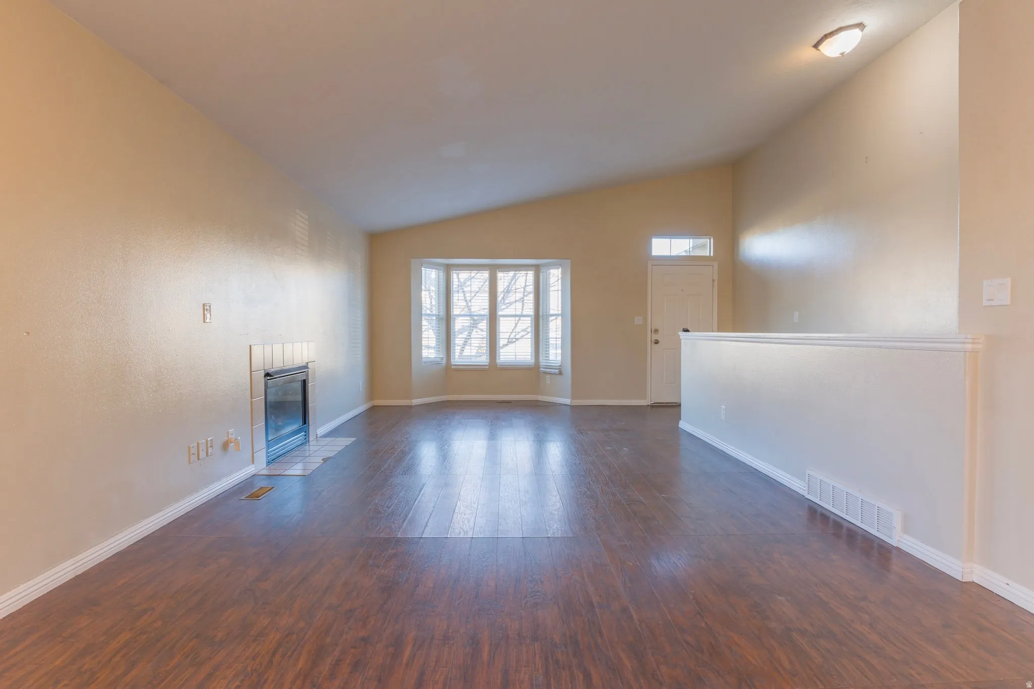 Unfurnished living room featuring lofted ceiling, dark wood finished floors, and a fireplace