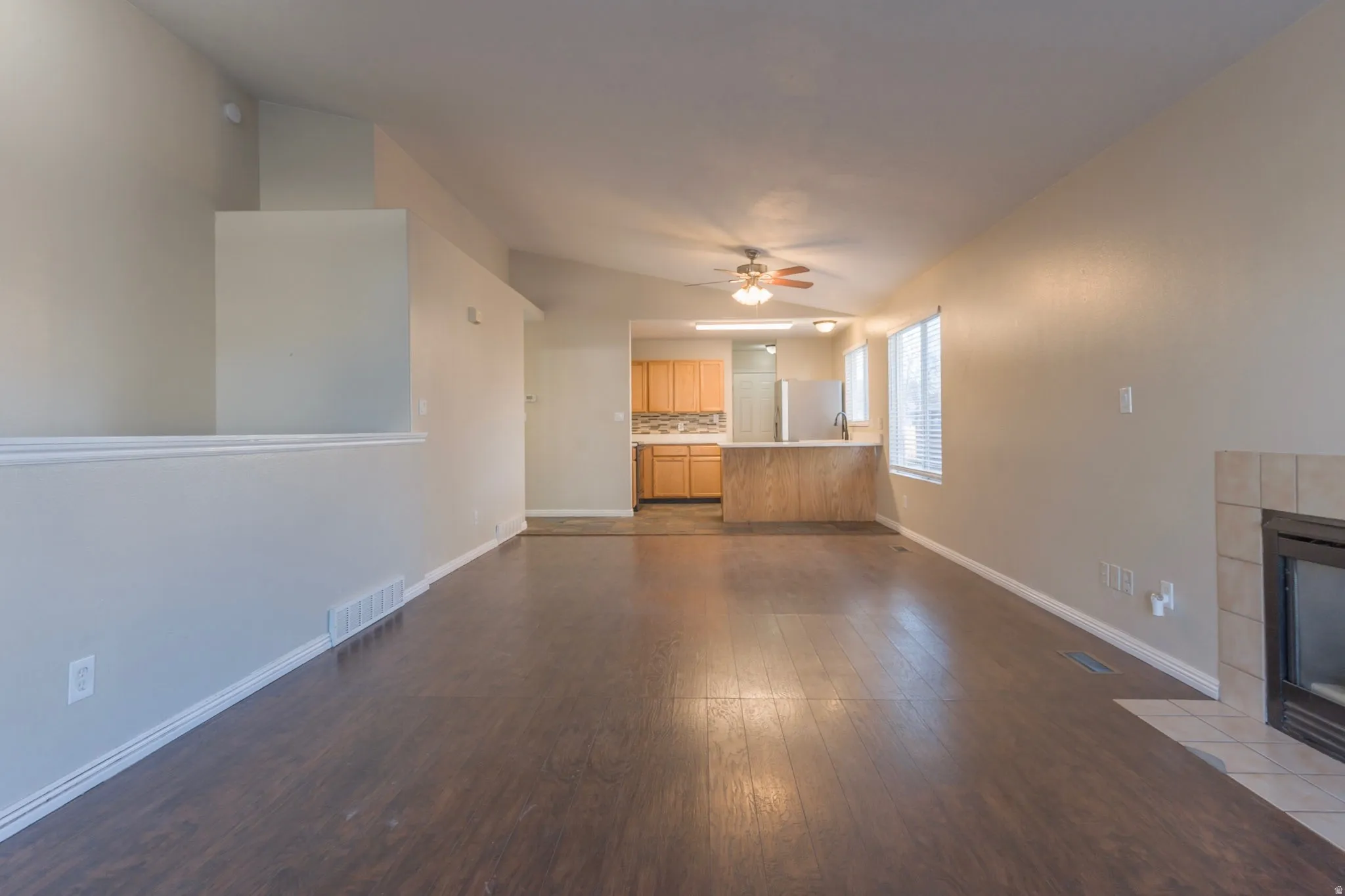 Unfurnished living room with a fireplace, dark wood-style flooring, lofted ceiling, and ceiling fan