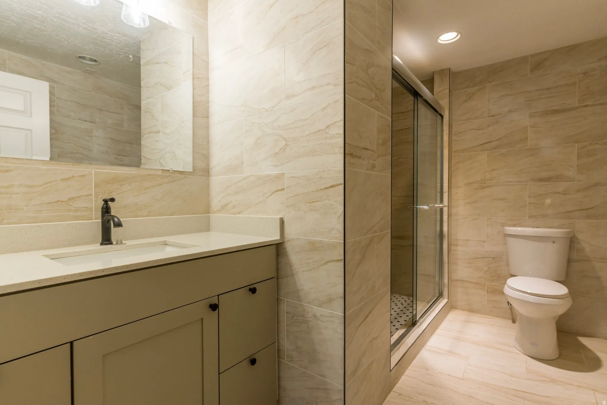 Full bath with tile walls, vanity, a stall shower, and recessed lighting