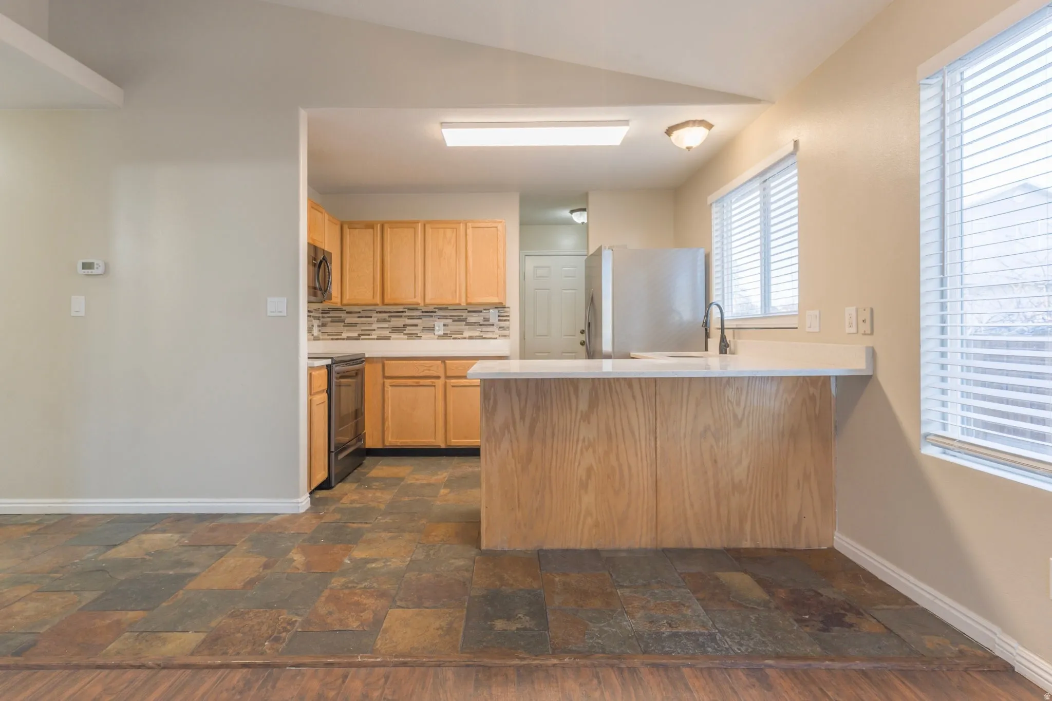 Kitchen featuring stone finish flooring, light countertops, a peninsula, appliances with stainless steel finishes, and backsplash