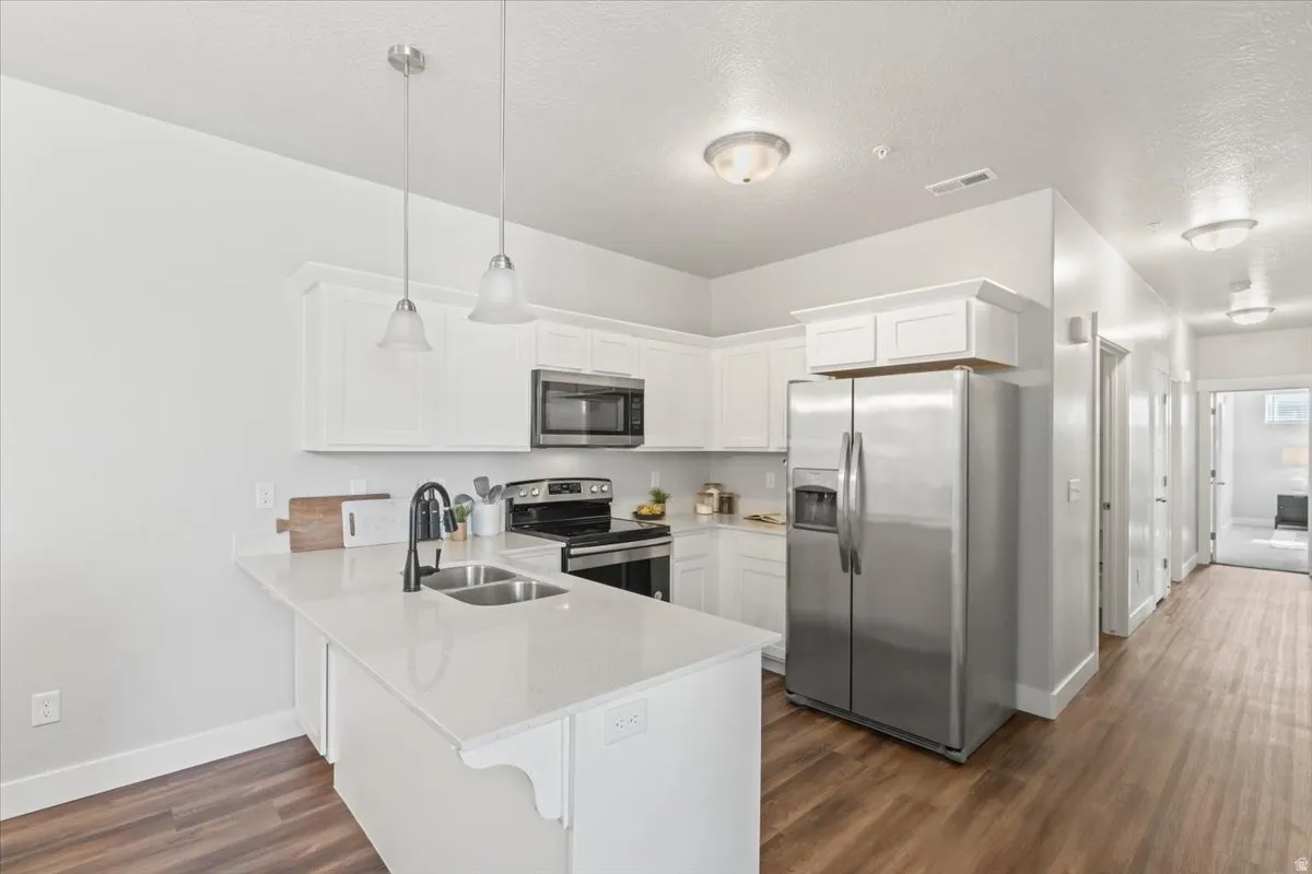Kitchen with appliances with stainless steel finishes, white cabinets, a peninsula, hanging light fixtures, and light stone countertops