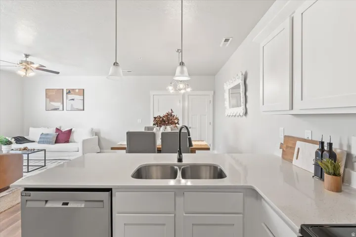 Kitchen featuring dishwasher, a peninsula, open floor plan, light stone counters, and pendant lighting