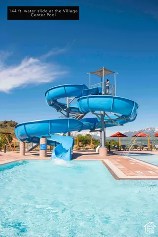 Curved water slide structure with a shaded top platform, integrated into a pool with a tiled perimeter, and featuring a mountain backdrop