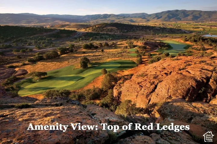 Expansive landscape featuring rugged red rock formations, lush green golf course fairways, scattered mature trees, and distant rolling hills
