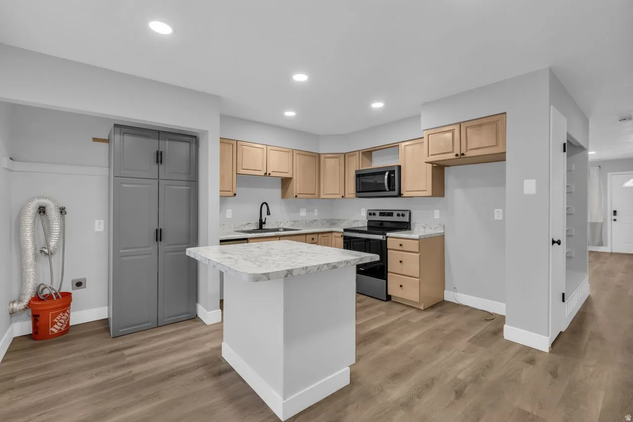 Kitchen featuring stainless steel appliances, light countertops, light wood-type flooring, recessed lighting, and a center island