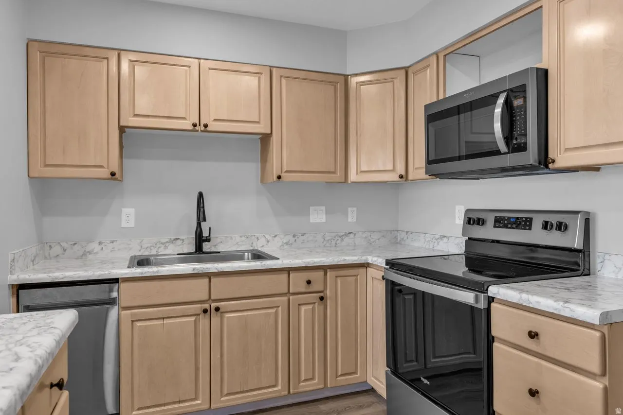 Kitchen featuring stainless steel appliances, light wood finish cabinetry, and wood finished floors