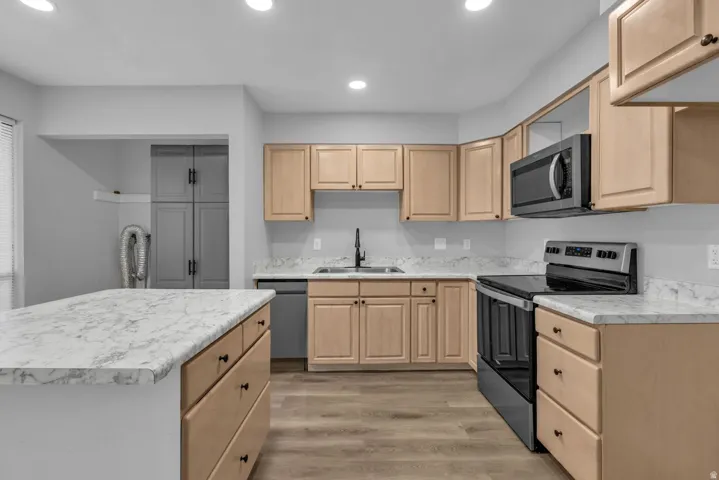 Kitchen with stainless steel appliances, light countertops, light wood finish cabinetry, light wood-style floors, and recessed lighting