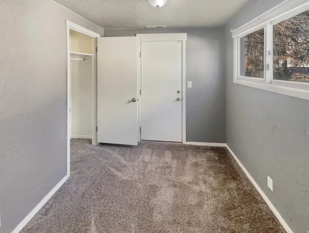 Carpeted room featuring light gray walls, a built-in closet with shelving and hanging rod, a white door, and a multi-pane window