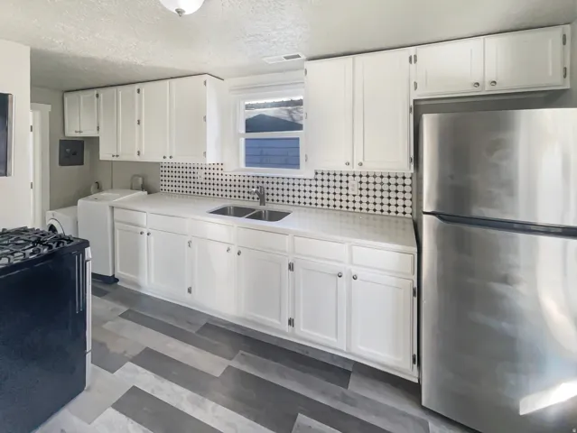 Kitchen featuring a stainless steel refrigerator, white cabinetry, a dual basin sink, and a black and white geometric tile backsplash