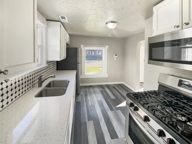 Renovated kitchen featuring white cabinetry, stainless steel appliances, a dual basin sink, and wood-finish flooring
