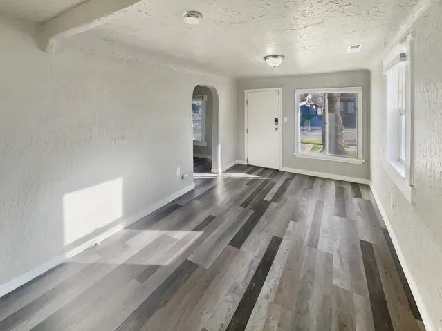 Spacious living area featuring contemporary wood-finish flooring, neutral wall tones, and ample natural light from multiple windows