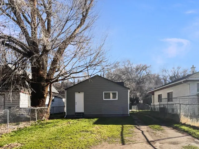 Rear exterior of the property featuring gray horizontal siding, white trim windows, and a white entry door