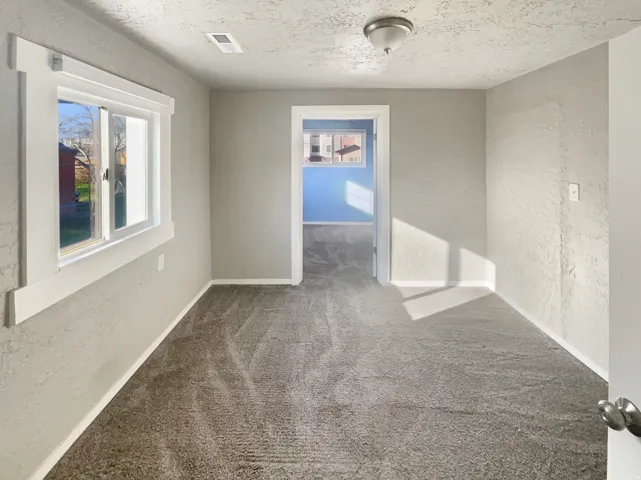 Plush gray carpeting throughout, featuring light gray walls, a window with white trim, and a ceiling-mounted light fixture