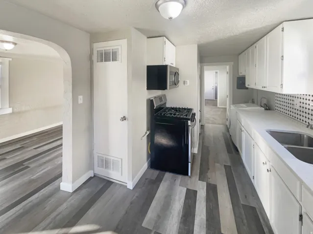 Galley kitchen featuring white cabinetry, light countertops, stainless steel double-basin sink, and a black gas range with microwave