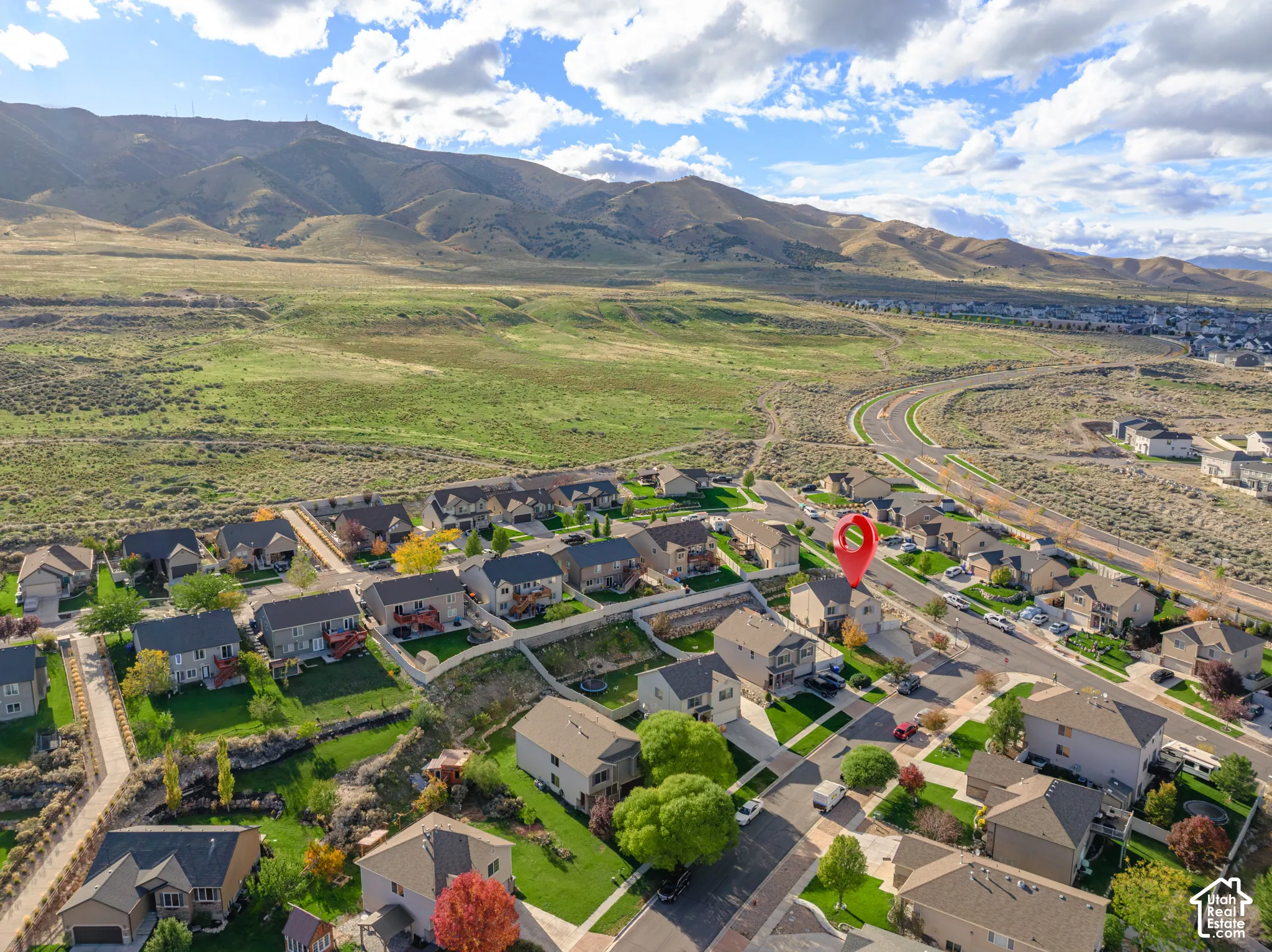 Aerial perspective of a suburban neighborhood featuring residential lots, asphalt paved streets, manicured green lawns, and a mountainous backdrop
