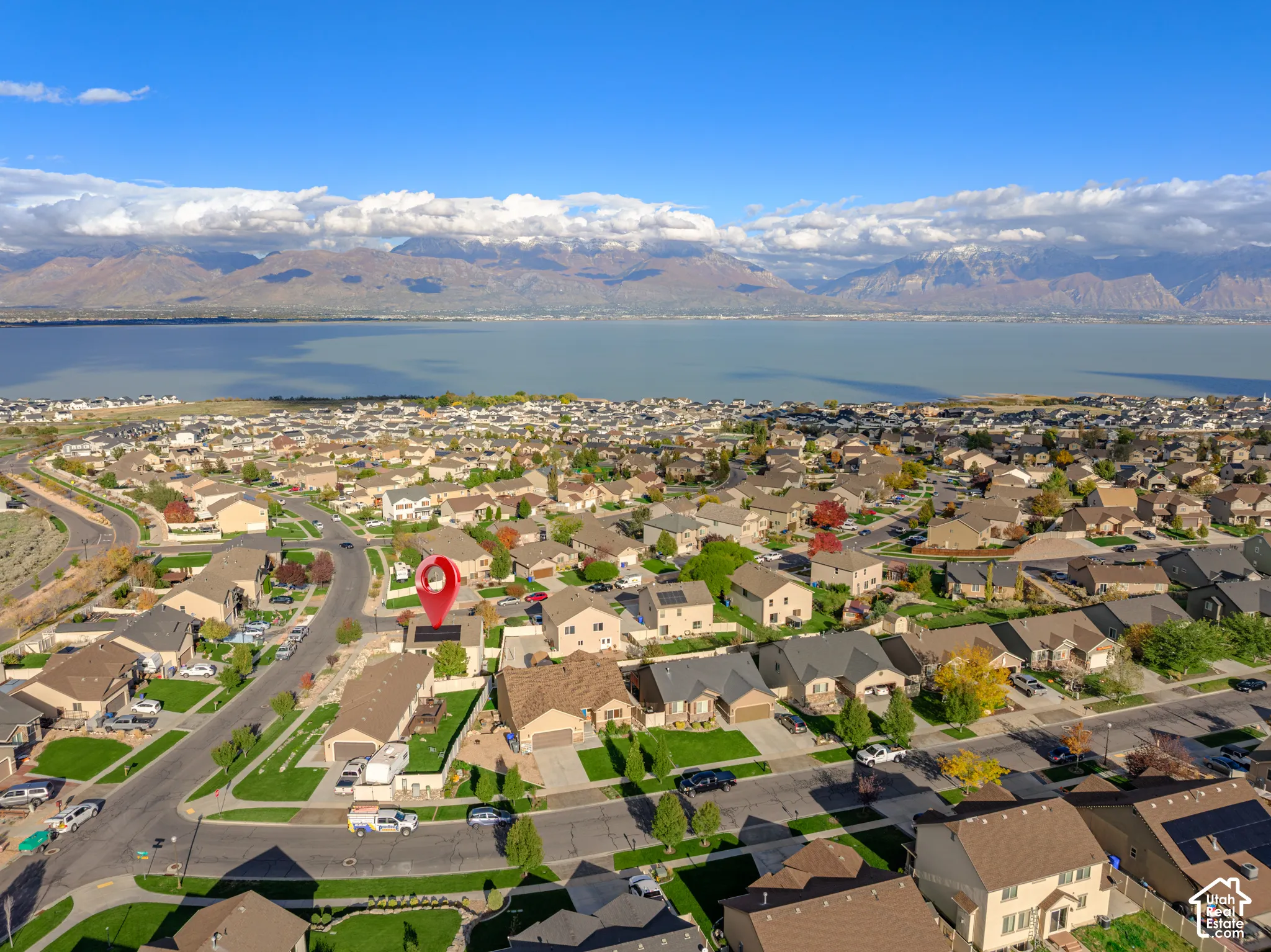 Aerial perspective highlighting a property with roof-mounted solar panels, situated in a suburban neighborhood featuring mountain and lake scenery