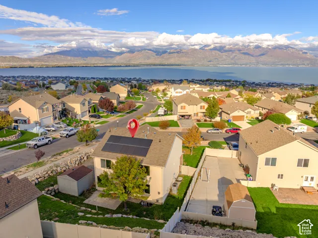 Aerial perspective featuring roof-mounted solar panels, a paved driveway, a storage shed, and a fenced backyard with landscaped terrain