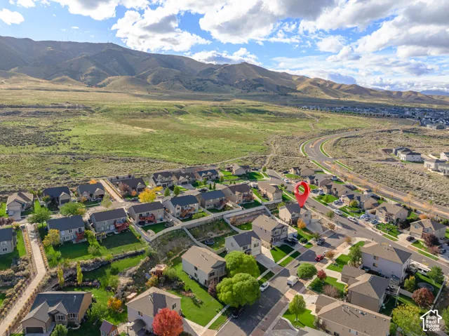 Aerial perspective of a suburban neighborhood featuring residential lots, asphalt paved streets, manicured green lawns, and a mountainous backdrop