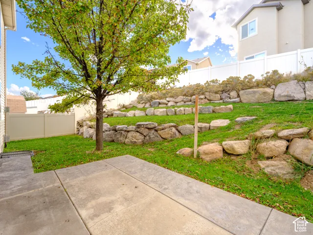 Rear yard featuring a concrete patio, tiered stone retaining walls, lawn area, and white vinyl privacy fencing