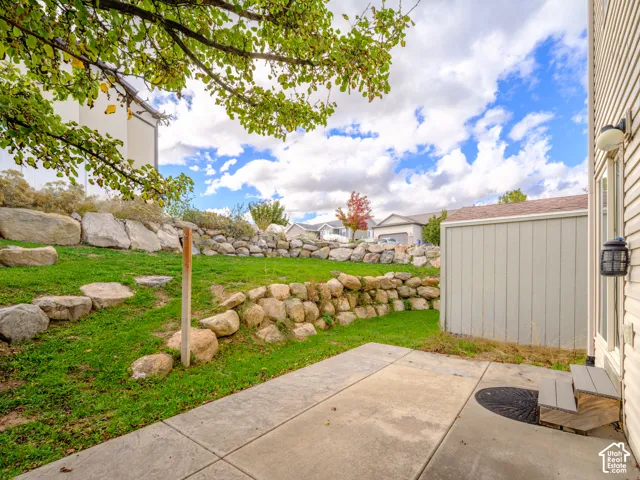 Concrete patio featuring tiered natural stone retaining walls, mature landscaping, and exterior wall-mounted lighting