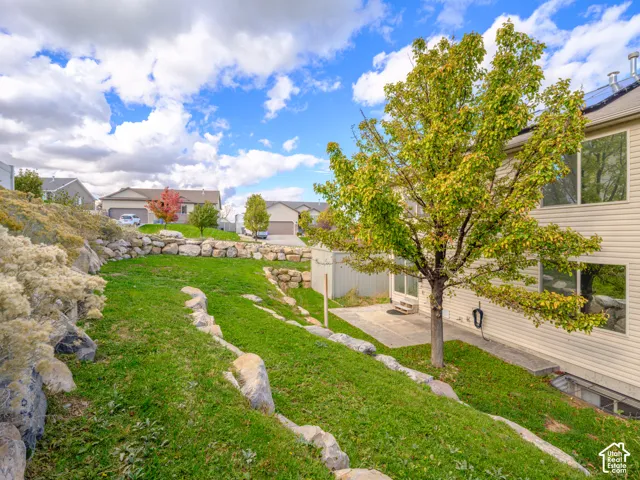 Tiered backyard featuring natural stone retaining walls, manicured lawn, mature tree, and concrete patio