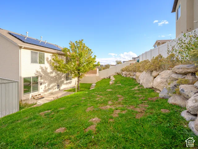 Exterior of the residence featuring roof-mounted solar panels, tiered natural rock landscaping, and a vinyl privacy fence