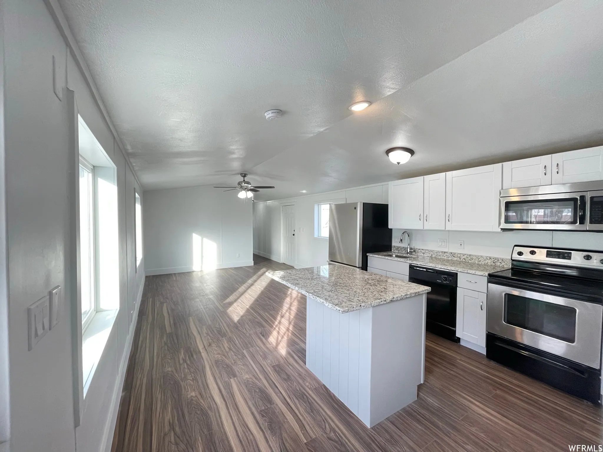 Kitchen with stainless steel appliances, open floor plan, white cabinets, dark wood-style floors, and lofted ceiling