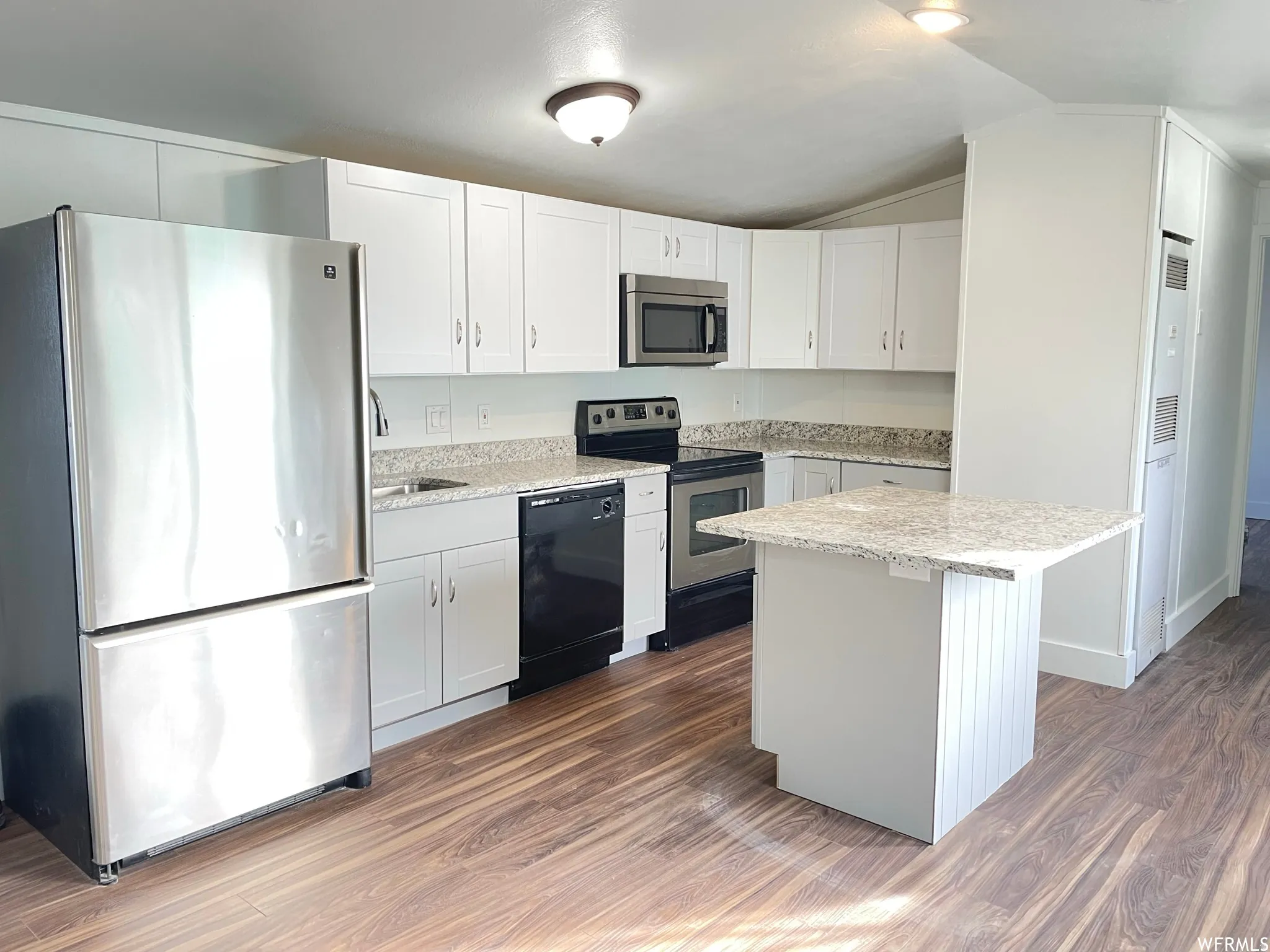 Kitchen featuring stainless steel appliances, white cabinetry, dark wood finished floors, lofted ceiling, and light stone counters