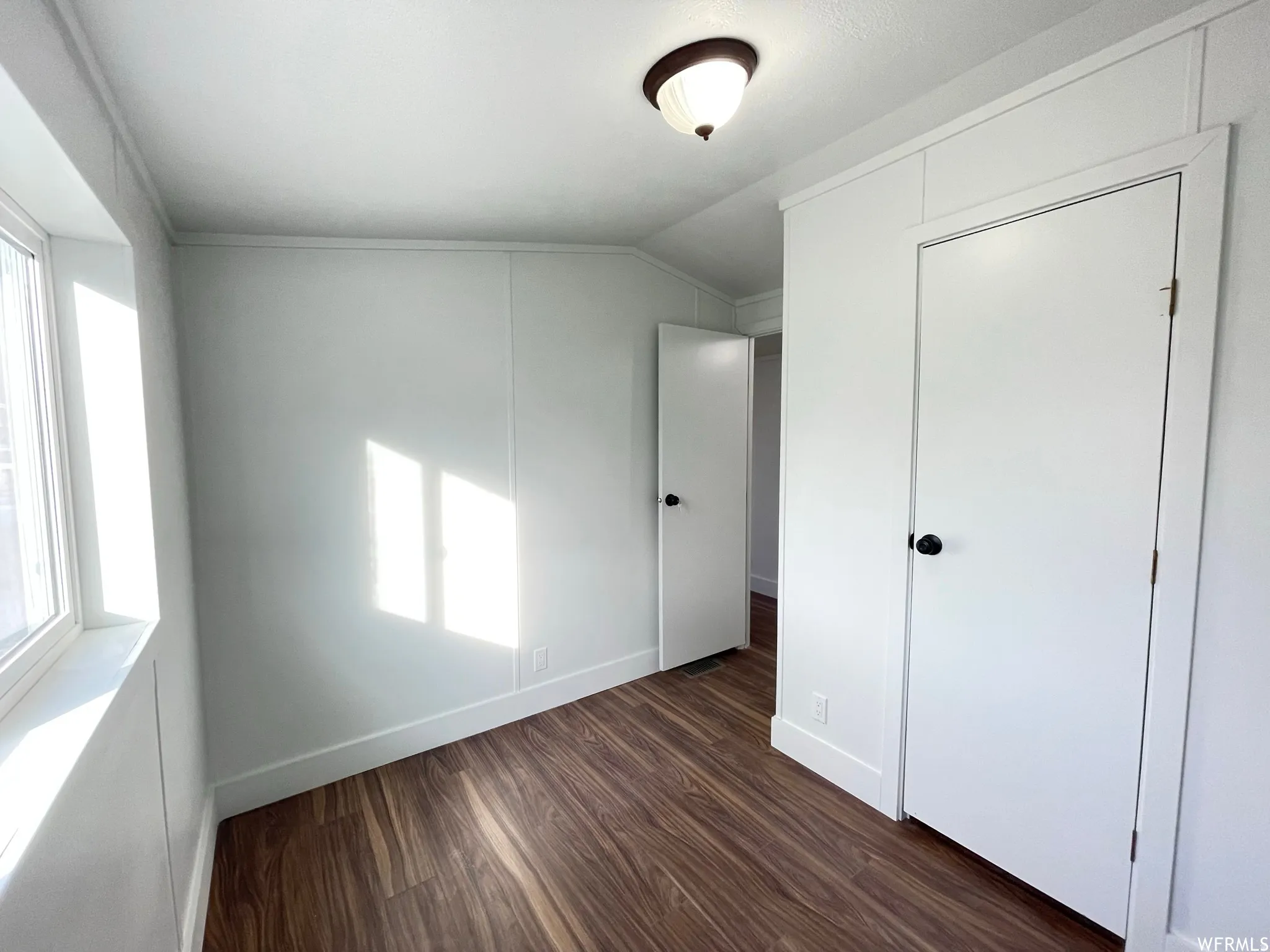 Unfurnished bedroom with multiple windows, dark wood-style flooring, and vaulted ceiling